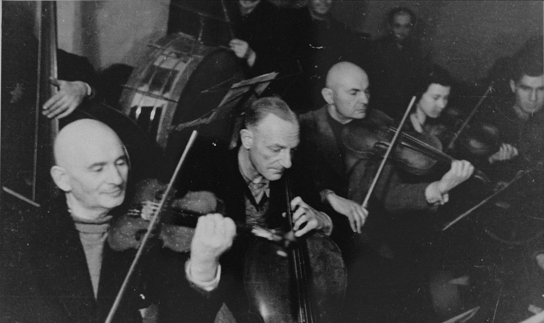 Performance of the Kovno ghetto orchestra.  

Among those pictured are: Mordechai Borstein (left), Korijski (middle), and Maya Gladstein (right).  Bornstein and Gladstein both survived and moved to Israel, while Korijski perished.