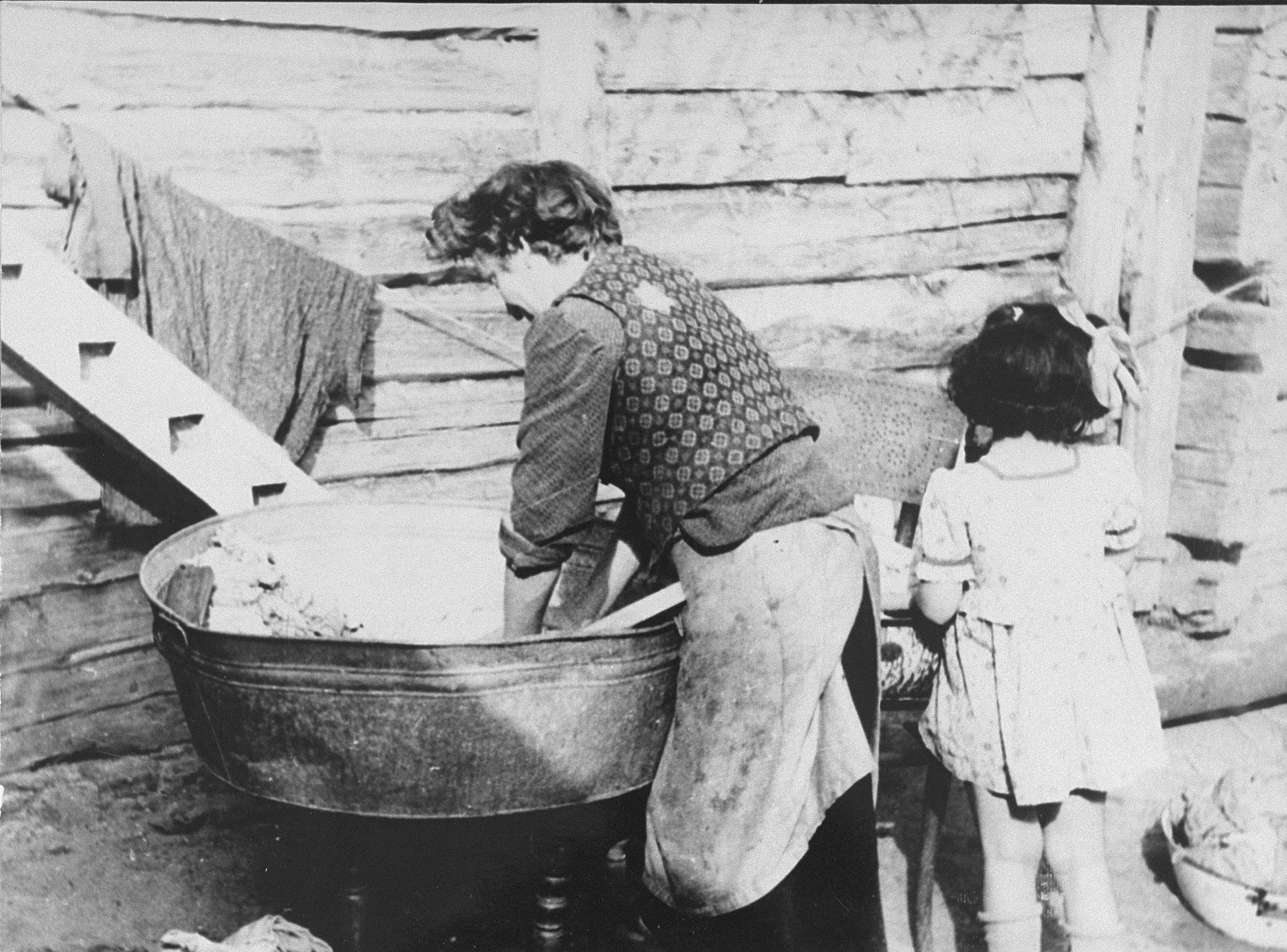 A woman does the washing in a basin outside at the ghetto laundry in the Kovno ghetto.

The laundry, which began operation on February 16, 1942, was one of 44 workshops in the ghetto.  It employed 41 persons, mostly women.  The laundry was very difficult to outfit initially since the ghetto had no sewer system or water mains, but ghetto engineers installed heating and water pipes to make it fully operational.  The laundry cleaned clothing and linens of German civil administrators, military and police.   In addition to providing labor for women who would have found it physically or personally difficult to join brigades outside of the ghetto, the laundry provided another benefit as well.  The ghetto was not allocated a soap ration.  Therefore, during the summer months, workers at the laundry frequently threw linen straight into the river for easy cleaning and channeled the saved soap to ghetto inhabitants.