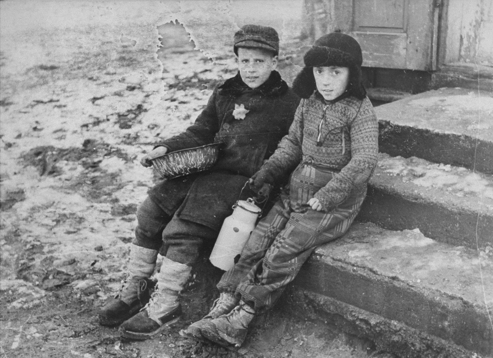 Portrait of two young boys with a milk can.

The caption by George Kadishon the back of the photo reads "Winter in the Kovno ghetto.  Early in the morning in line for soup".