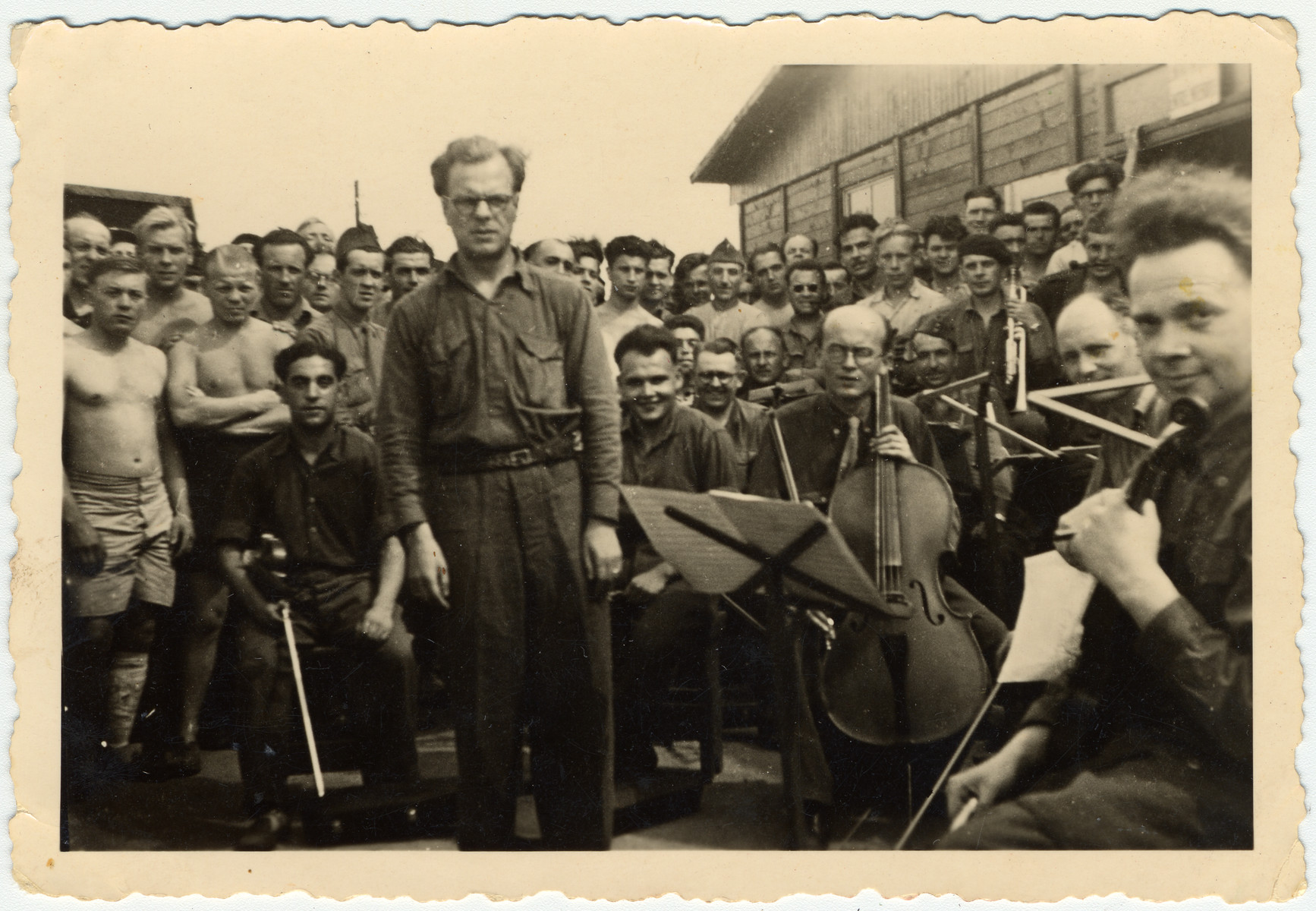 Performance by the prisoner orchestra at Stalag VIIIA in front of the infirmary.

Fernand Carion, a Belgian musician and prisoner-of-war is conducting.  Max Beker (concert master) is pictured sitting on the left.