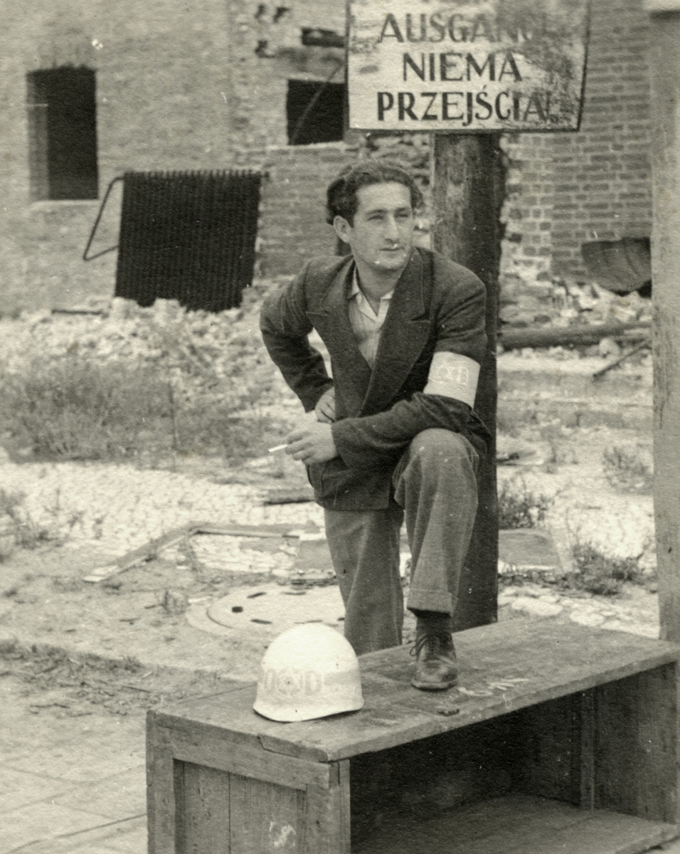 Nathan Schwarzfeld, a Jewish policeman in the Tempelhof displaced person camp, poses wearing an armband with his police helmet next to him.