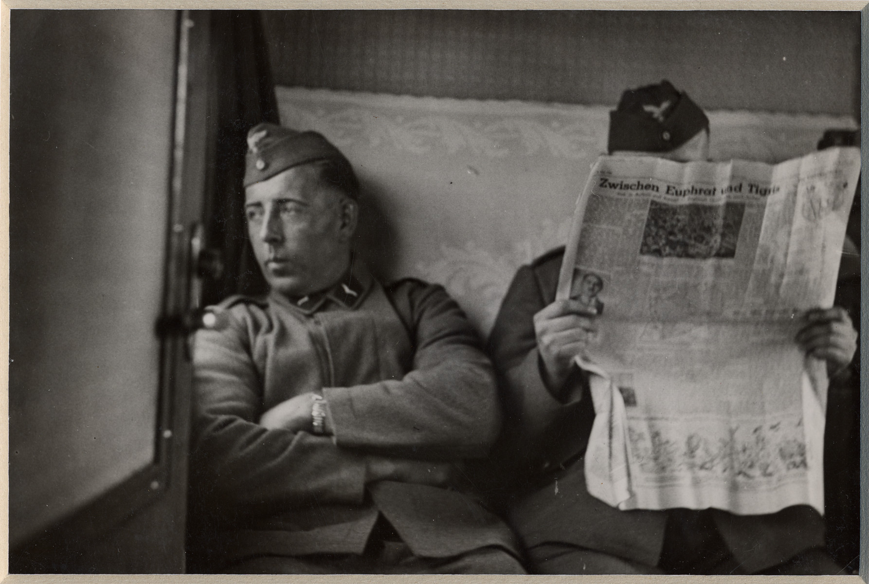 Two German men sit in a train car; one is reading a newspaper.

The back page is a story entitled "Between the Tigres and the Euphrates".