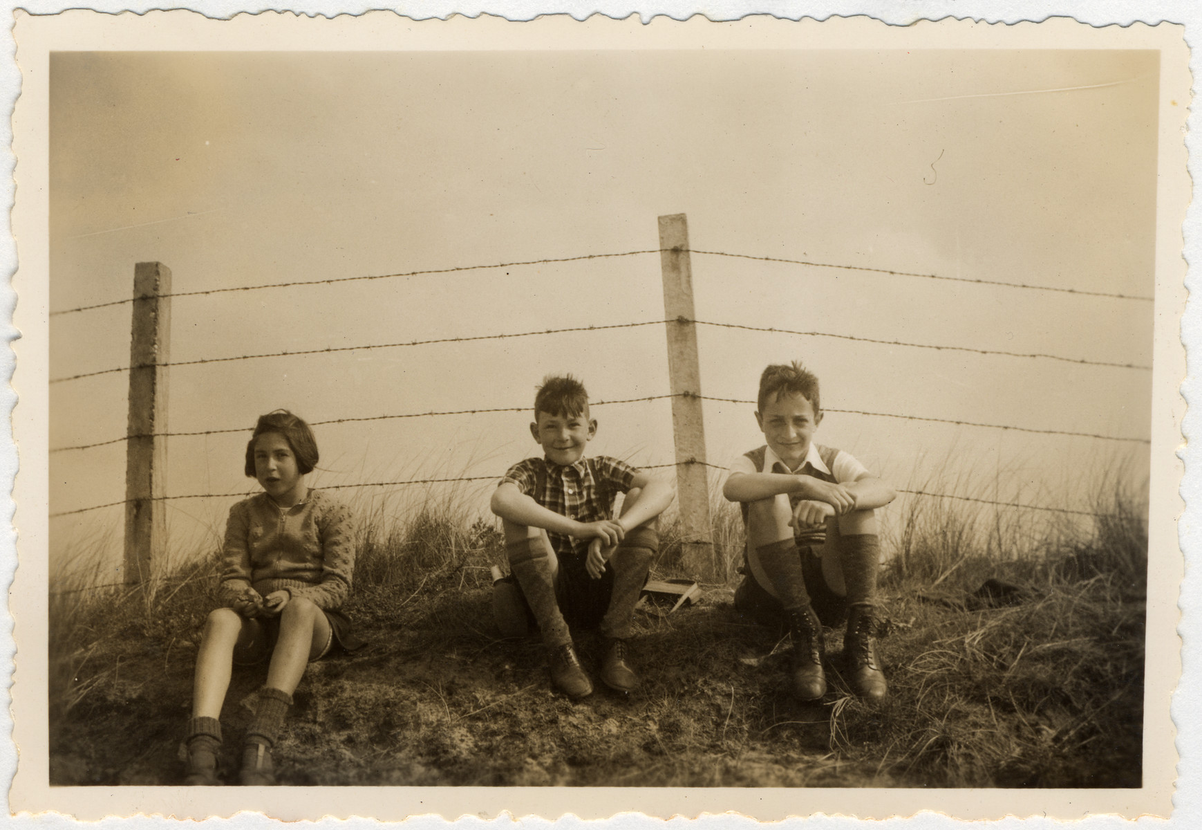 Three children rest during a bike ride to the coast which is blocked off with barbed wire in anticipation of the coming war.

Pictured are Clary and Jaap Vromen and a friend.