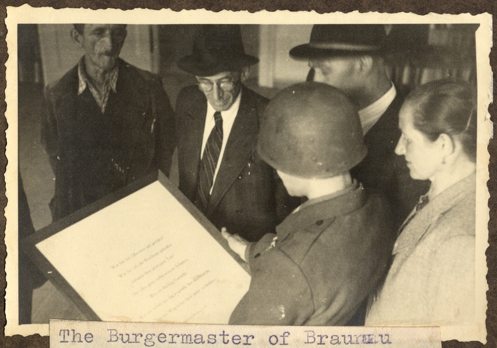 Joseph Eaton, an American soldier and German-Jewish emigre, sets up a display of biblical quotations in the home where Adolf Hitler was born.

The original caption reads: "The Burgermaster of Braunau watches the text being hung up."