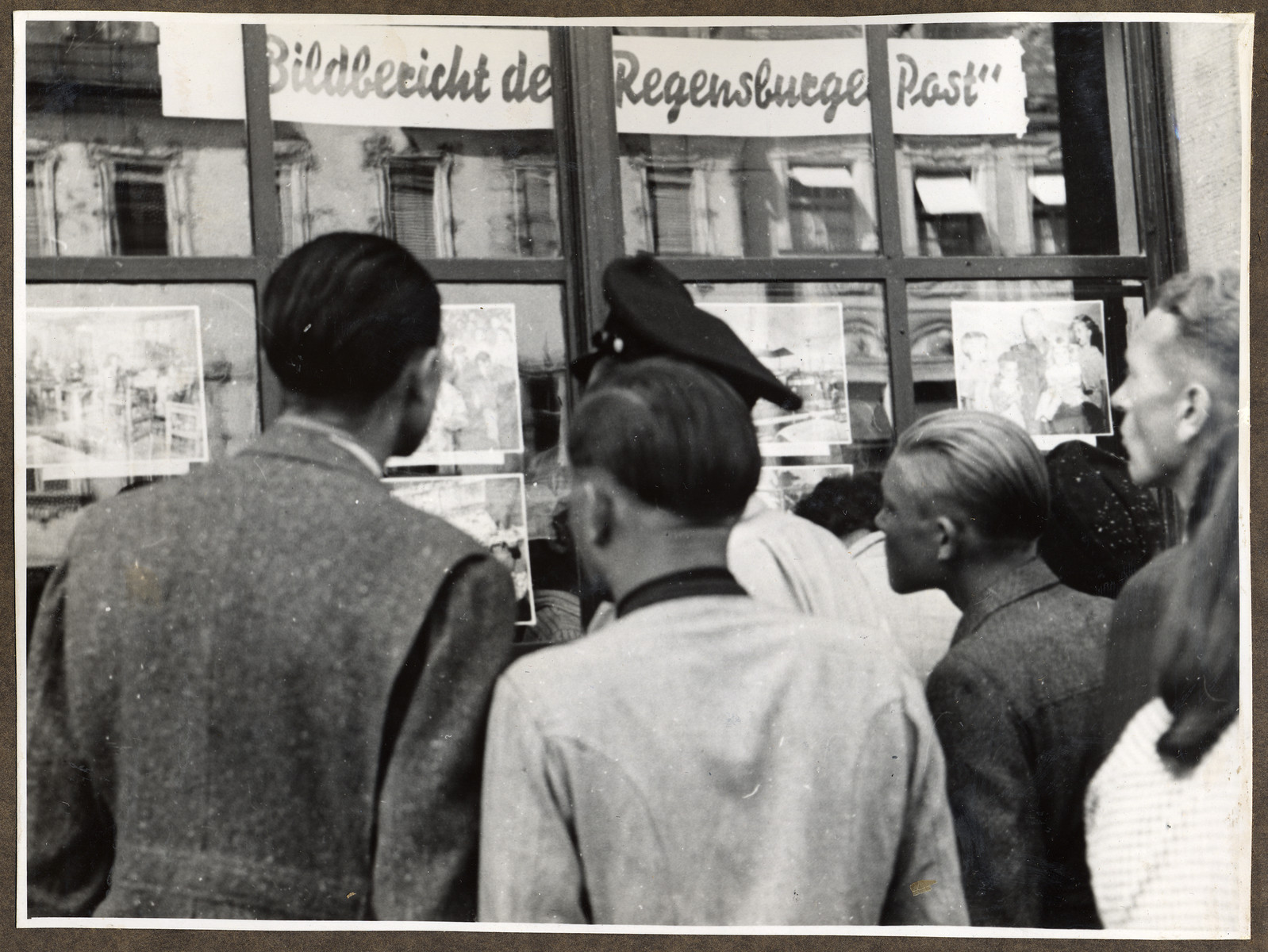 German civilians study the weekly photo news exhibit of the American-printed Regenburg Post in Straubing. 

The newspaper was edited by the donor, Joseph Eaton.
