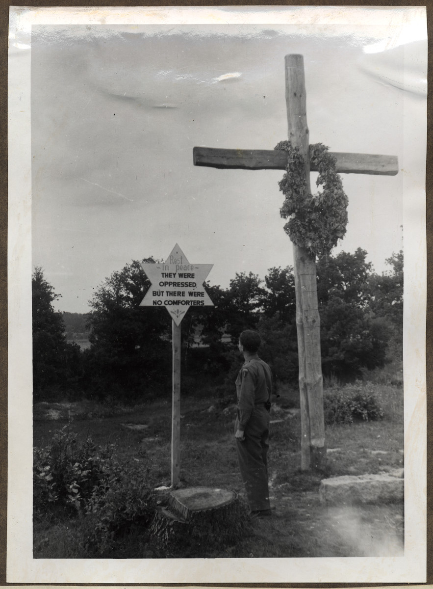 An American soldier studies a grave marker on the sight of a mass grave of death march victims.

The original caption reads: "A mass grave of Concentration Camp inmates murdered as the SS was chasing them along the roads, away from the persuing Americans - when liberation was so near".