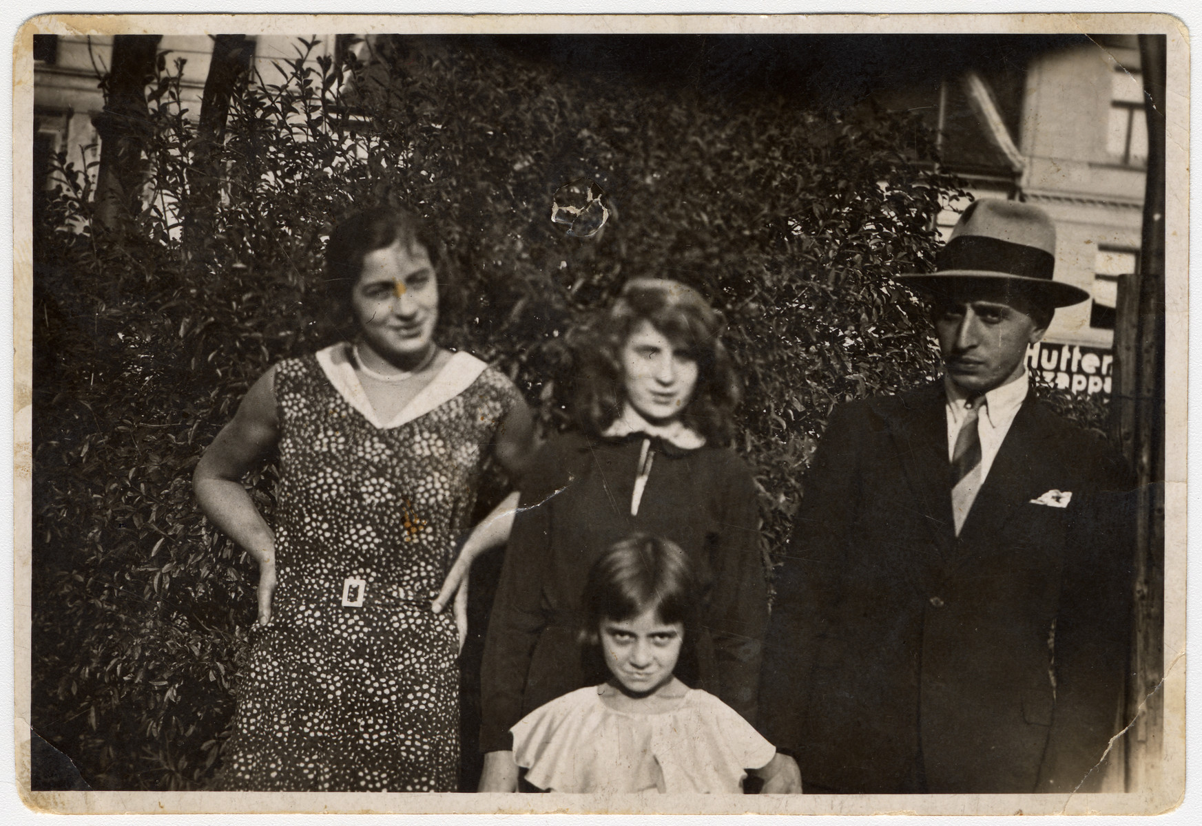 A family poses outside on a city street in Budapest.

Pictured are Anges Biel's mother's (Katalin) family. From left to right are siblings Gizi, Teri, and Jeno. The little girl on the bottom row is Ibolya.