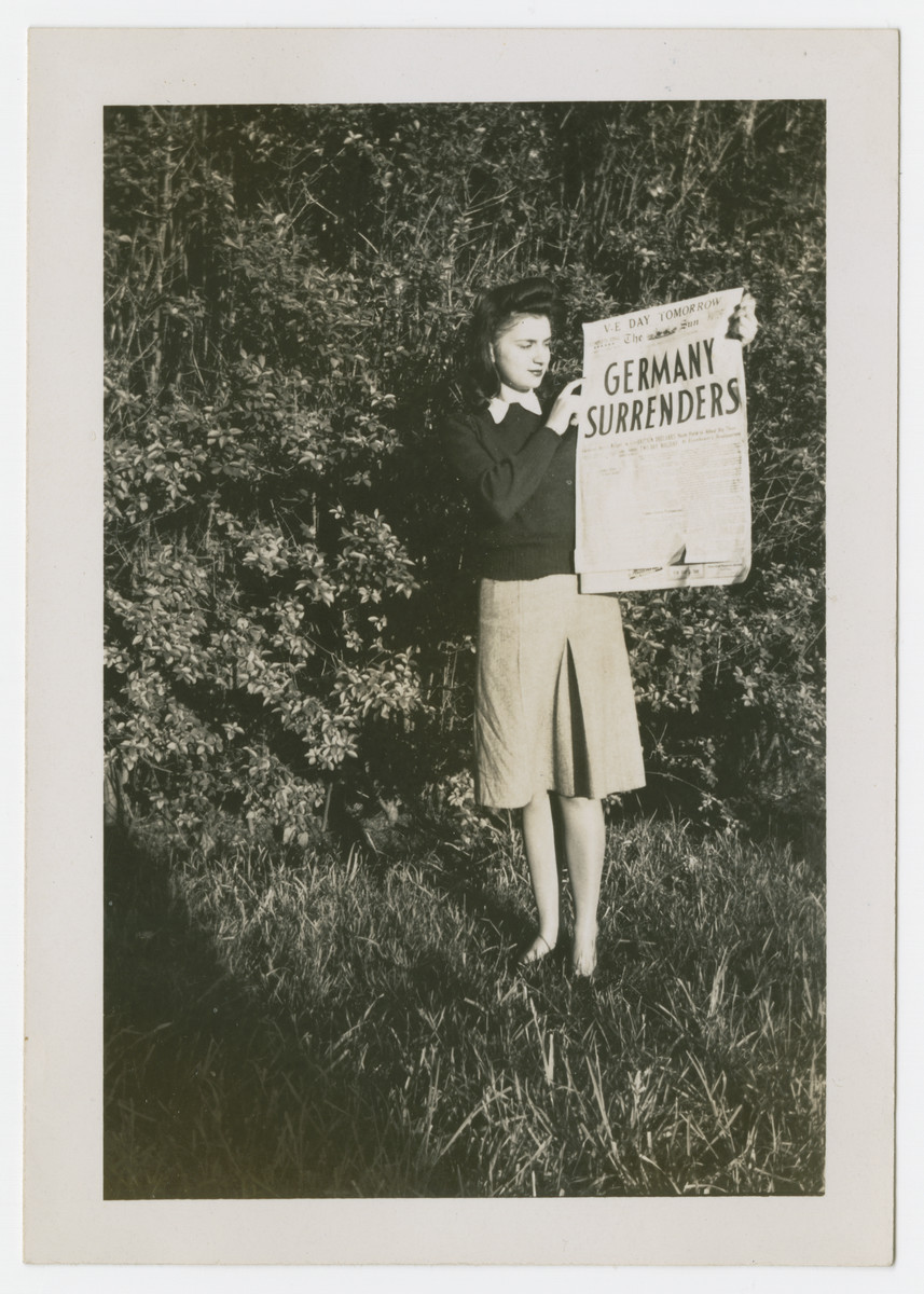 Mary Berg holds up a newspaper announcing the surrender of Germany.