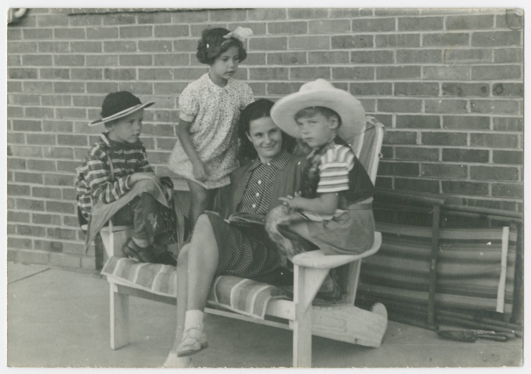 Mara Vishniac sits on a bench surrounded by three younger children.

Ruth Rahn is to her left.  The Rahns and Vishniacs had been friends in Berlin and both immigrated to the United States to escape the Nazis.

The original caption reads: "Mara and her kindergarten.  Ruth dressing "girlishness" (see bow in hair) probably to impress the fierce cowboys."