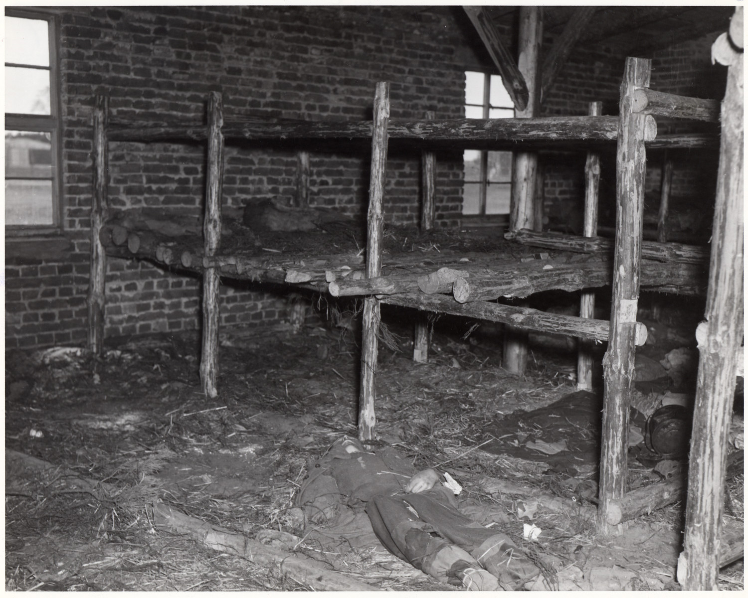 The body of a starved prisoner lies on the floor of a barrracks of the Woebbelin concentration camp.

The original caption reads:: "Wobblin Concentration Camp (No.8 of 13 photos).  he camp, recently captured by troops of the U.S. Ninth Army, had many prisoners who starved to death. Here one lies dead on the floor in the living quarters of the prisoners.

82nd Airborne Div., Wobbelin, Germany. 5/4/45."

Original caption from donated photograph:  "A dead inmate lies on the floor of one of the filthy "bedrooms" of the concentration camp at Webblin.  U.S. troops liberating this atrocity center described it as one of the worst in Germany.  Hundreds of dead prisoners were found piled up in one building and hundreds were discovered in crude, hastily dug pits.  Into one mass grave the Germans had tossed the corpses of 300 slave laborers of various nationalities.  Of the original 4,000 prisoners, it is estimated that 150 died daily, mostly from inhuman treatment and starvation.  German residents of the area were ordered to exhume the bodies and provide respectable burial."