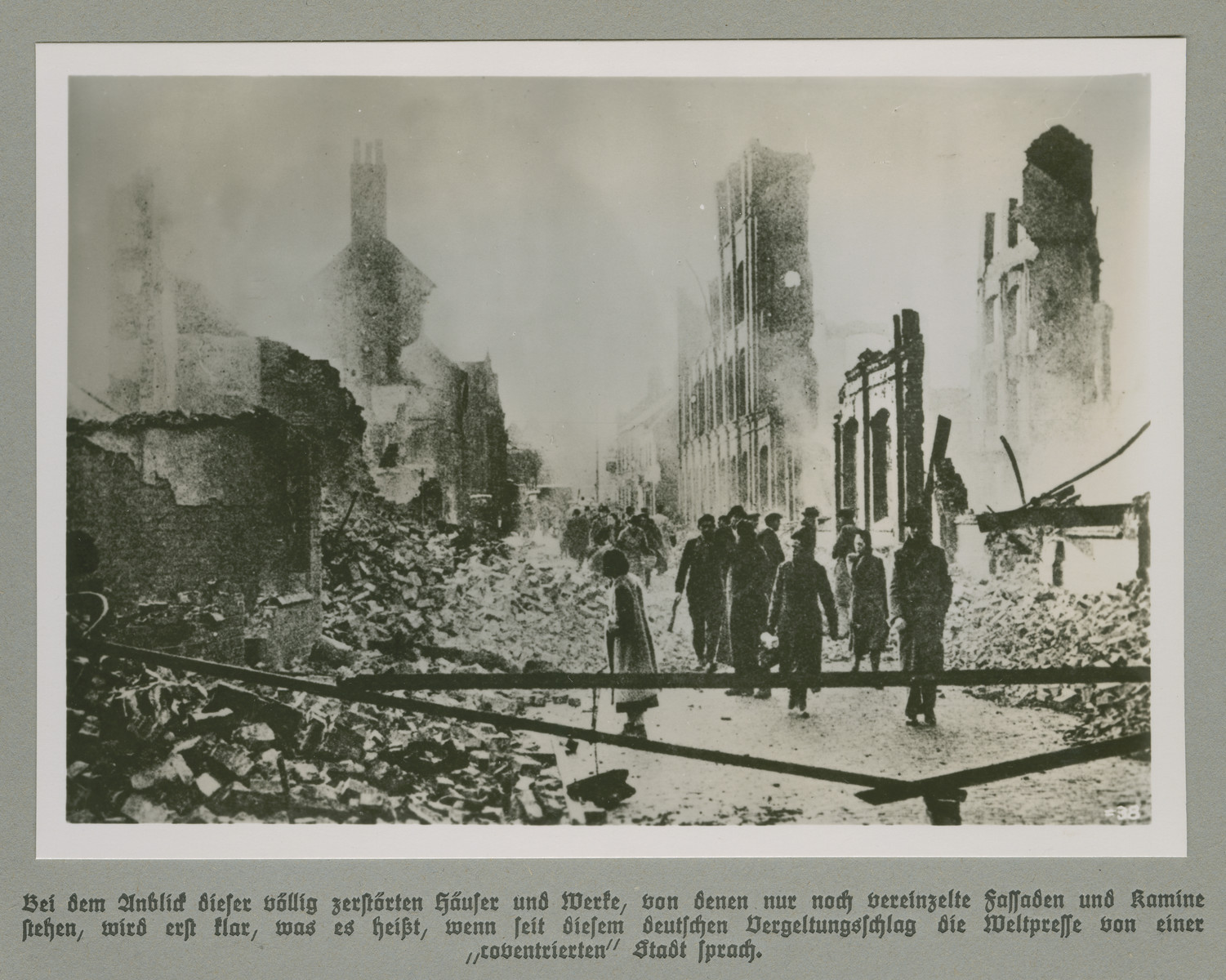 Men and women walk through a city quarter reduced to rubble.  

Original caption reads: Upon sight of the completely destroyed houses and industrial plants it first becomes clear what it meant, when since the begining of this German retaliation, the global press has spoken of a "coventried" (razed) city.