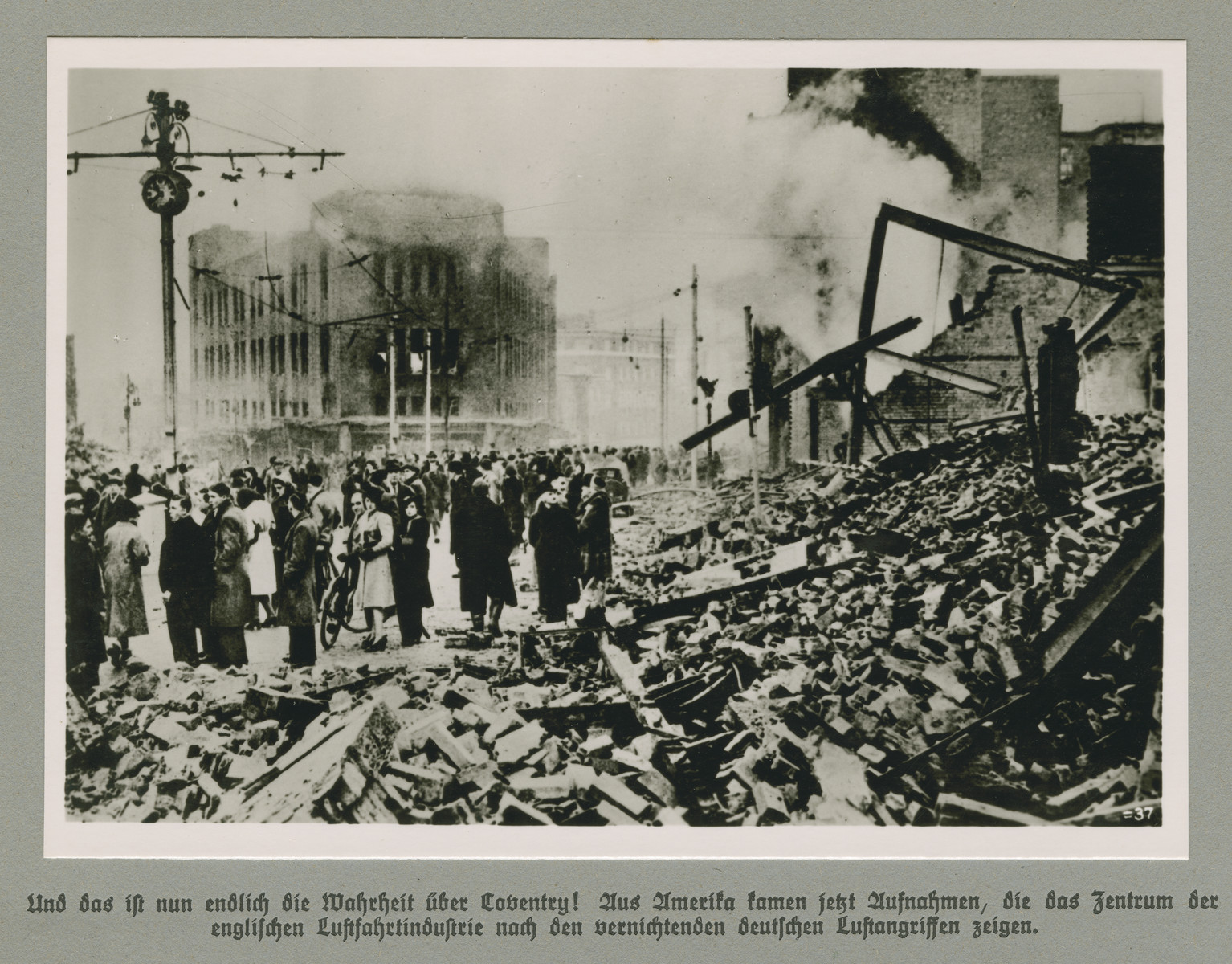 Men and women stand behind piles of rubble in a bombed out city quarter. 

Original caption reads: And finally the truth about Coventry! Images have come out of America that depict the center of the English aircraft industry after the devastating German airstrikes.