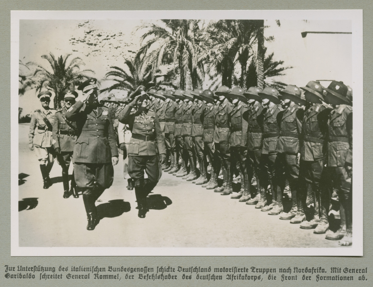 High ranking military personnel walk past and salute troops.

Original caption reads: Germany sent motorized troops to North Africa in support of its Italian allies. General Rommel, the commander of German troops in North Africa, walks with General Garibaldo astride the front line of the formation.