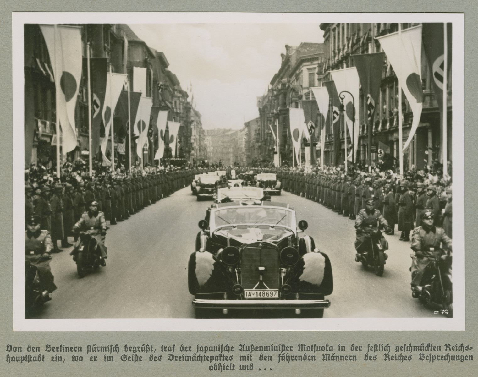A motorcade proceeds down a Berlin street lined with Japanese and Nazi flags.

The original caption reads:  Welcomed enthusiastically by the people of Berlin, the Japanese Foreign Minister Matsuoka arrives in the festively adorned capital  where he met and held talks with the Reich's leading men as a representative of the Tripartite Pact, and... 

(Caption continues with associated image on WS# 75979)