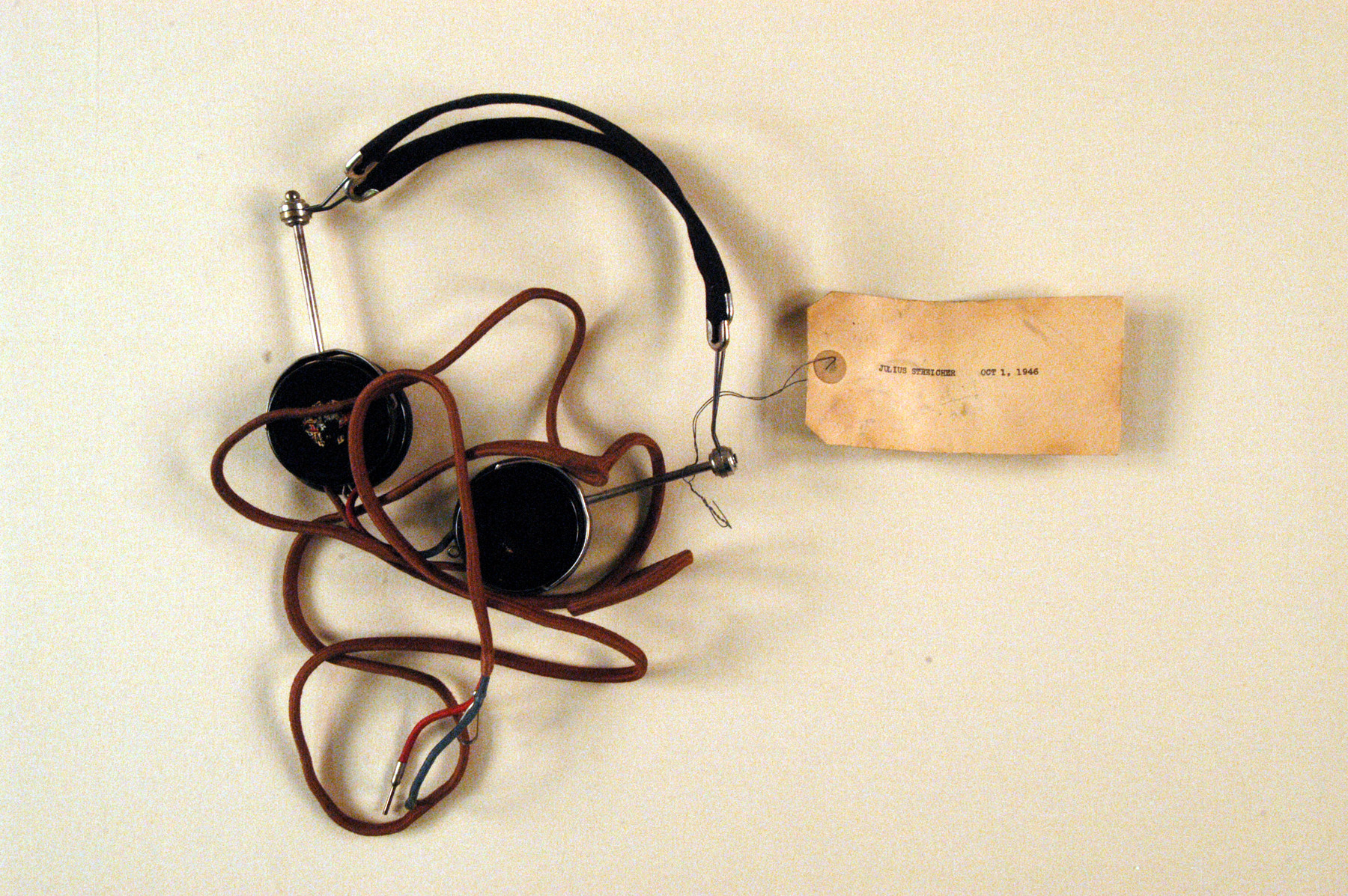 Headphone worn by Julius Streicher, former editor of Der Stuermer, a defendant in the International Military Tribunal in Nuremberg.  A tag with his name is attached to the headphone.