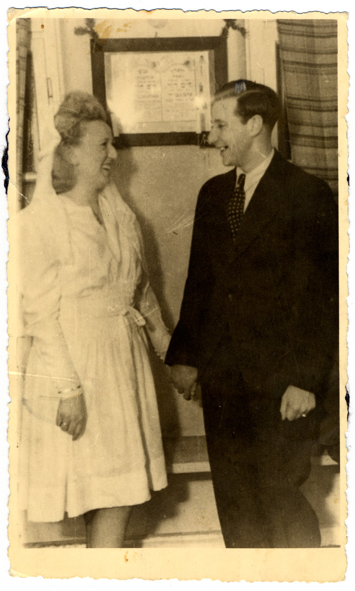 Ruth and Harry Posmantier look at one another on their wedding day.  They are standing in front of his father's memorial.