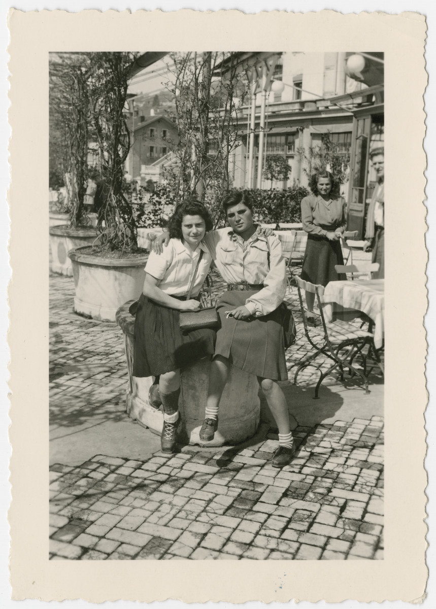 Two women who came to Switzerland on the Kasztner tranport pose together at an outdoor cafe.

Pictured in front are Berta Rubinsztajn (left) and ? Moskovitz (right).  Eva Weinberger is standing behind them at the back right.