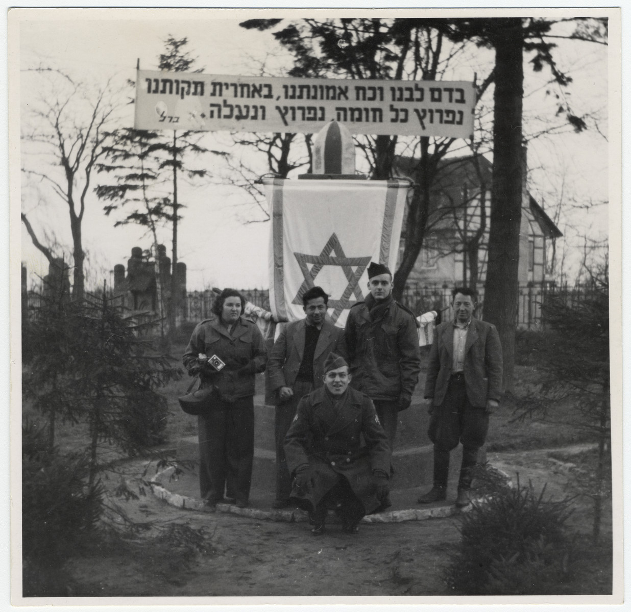 Five people, including members of the Frankfurt Jewish GI Council pose in front of a memorial in a German displaced persons' camp.

Crouching in front in Asher Hirsh, a German Jewish refugee who joined the US Army.

The Hebrew banner reads: "With the blood of our hearts, and the strength of our faith, with our last hopes, we will breach every wall, breach and ascend."