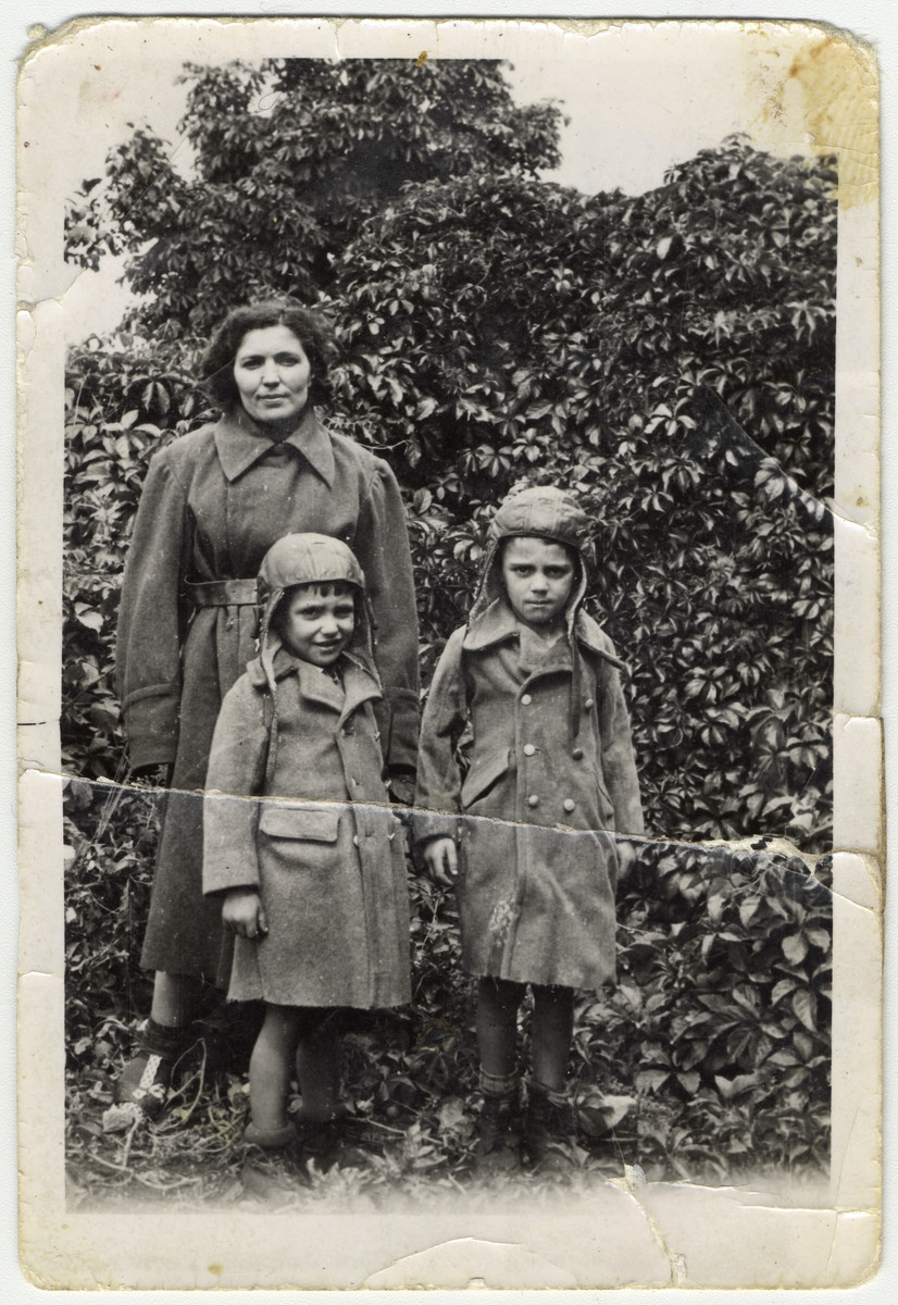 Shanke Minuskin stands outside in the Zeilsheim displaced persons' camp with her two sons, Kalman and Henik.  The boys are wearing coats their mother sewed for them in the forests made from the coat of a dead German.