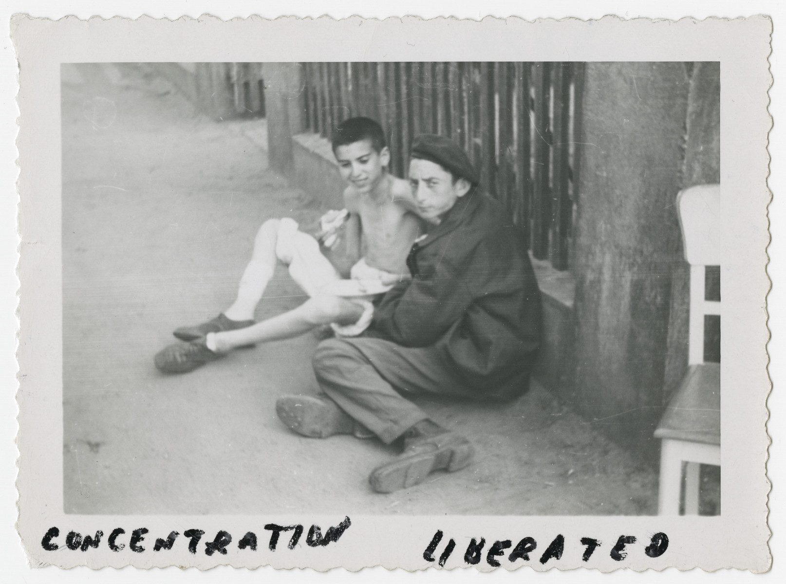 Two young prisoners from the Woebbelin concentration camp lean against a fence after liberation.  

The one farthest from camera was interned at age 15 and was liberated at age 18.  He weighed 60 lbs when liberated.