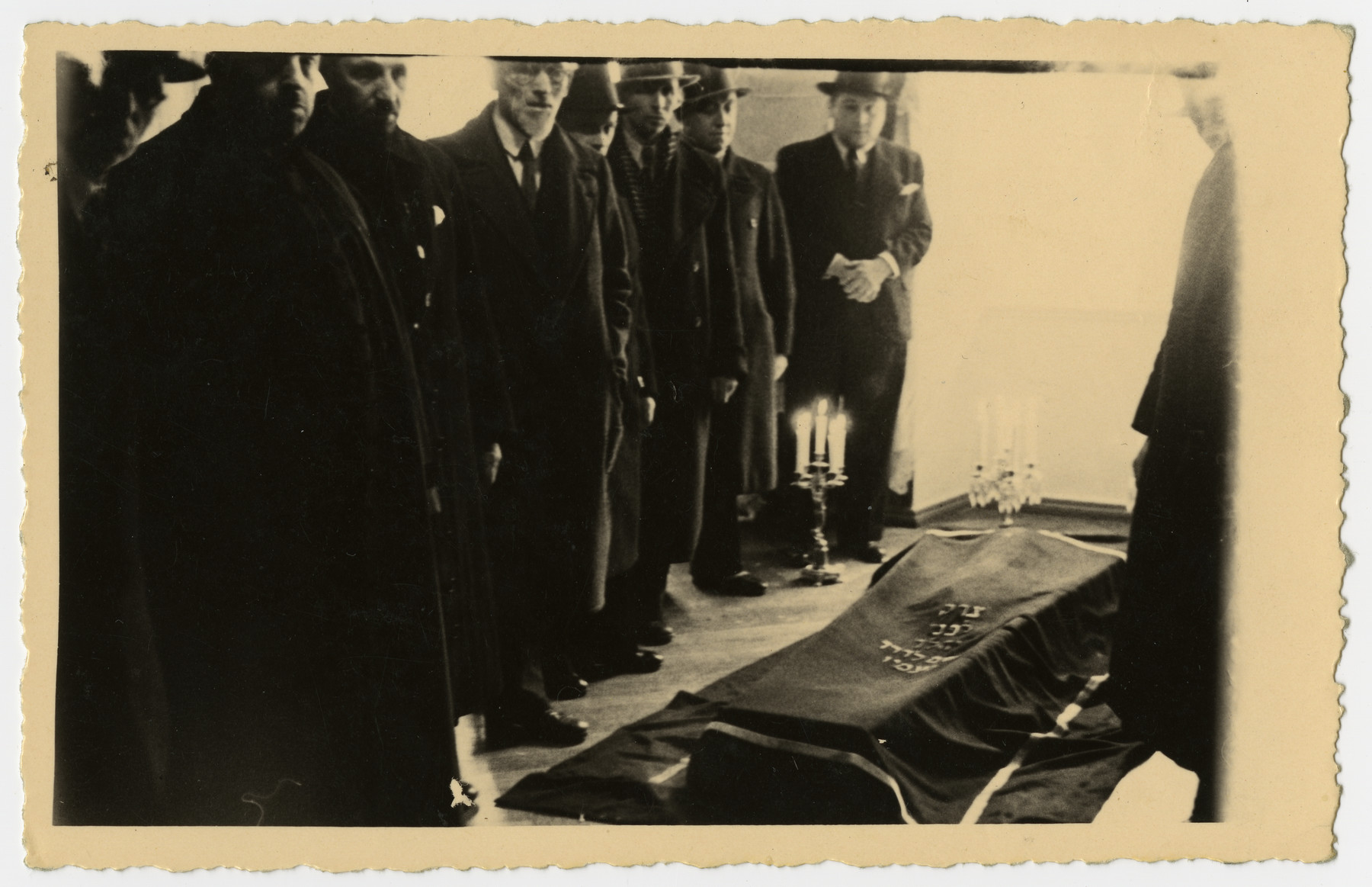 The body of Freida Albin lies in state prior to the funeral.

A group of men stands in attendance.