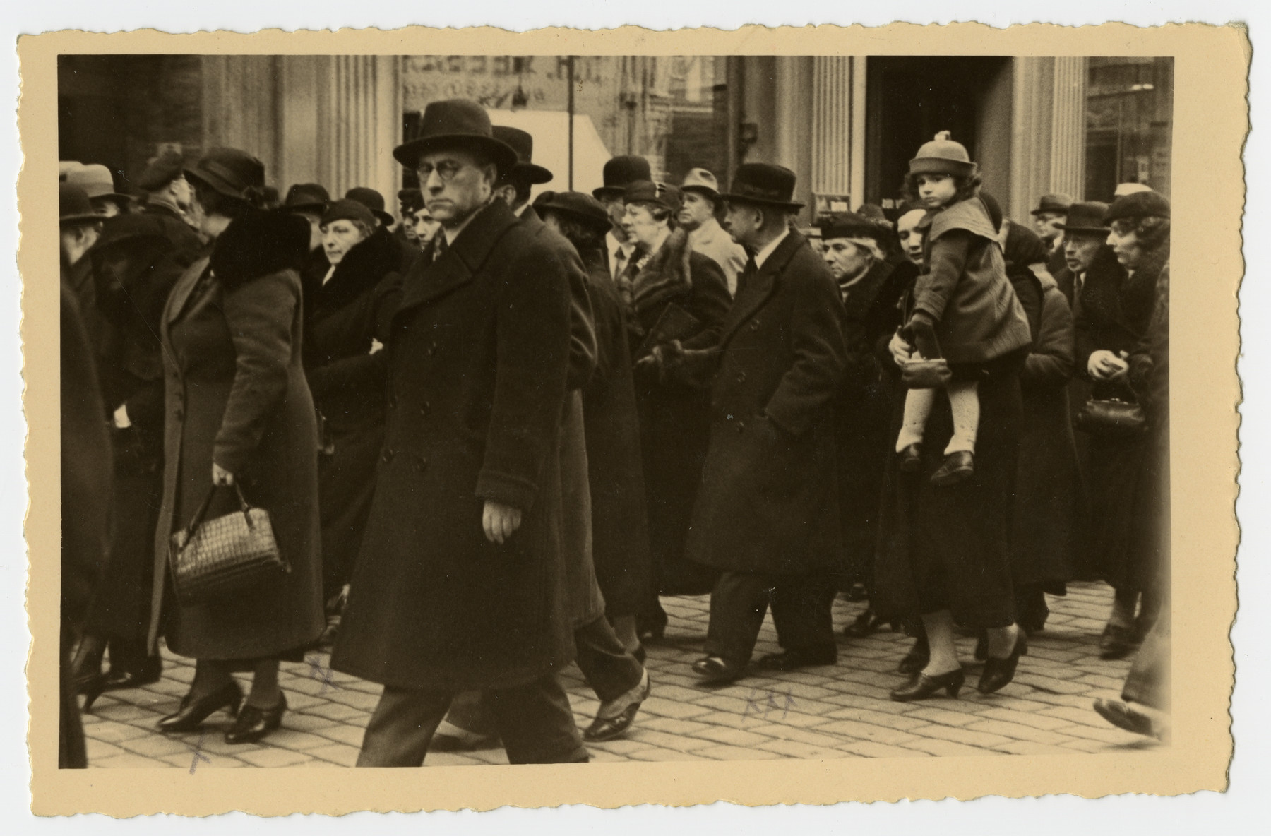 Mourners march down a street of Riga during  the funeral procession for Freida Albin.

Among those pictured are Aunt Zilla (wife of Uncle Aron); Aunt Berta Opapa; Aunt Zerna, behind her Bronja's head, and Mr. Mahler.