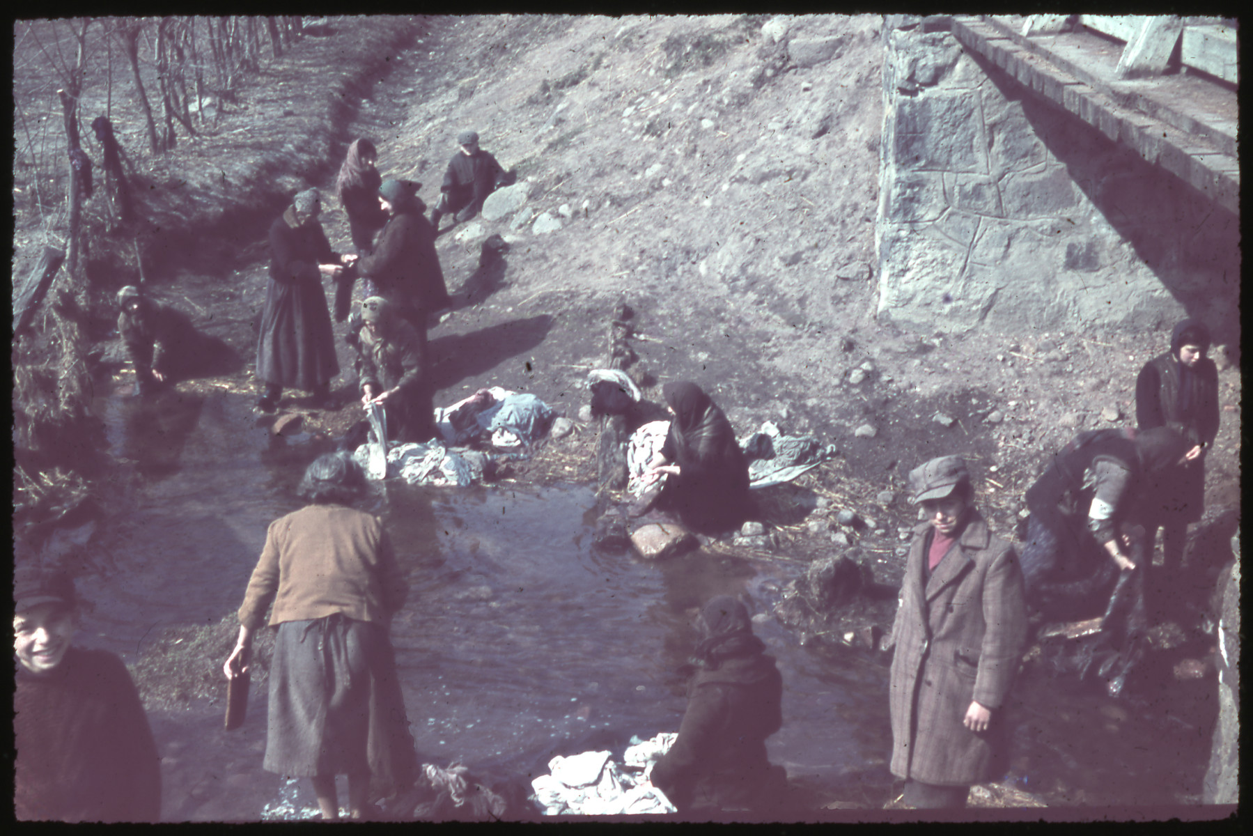 Women, some wearing armbands, wash their laundry in the Zagorzonka River.