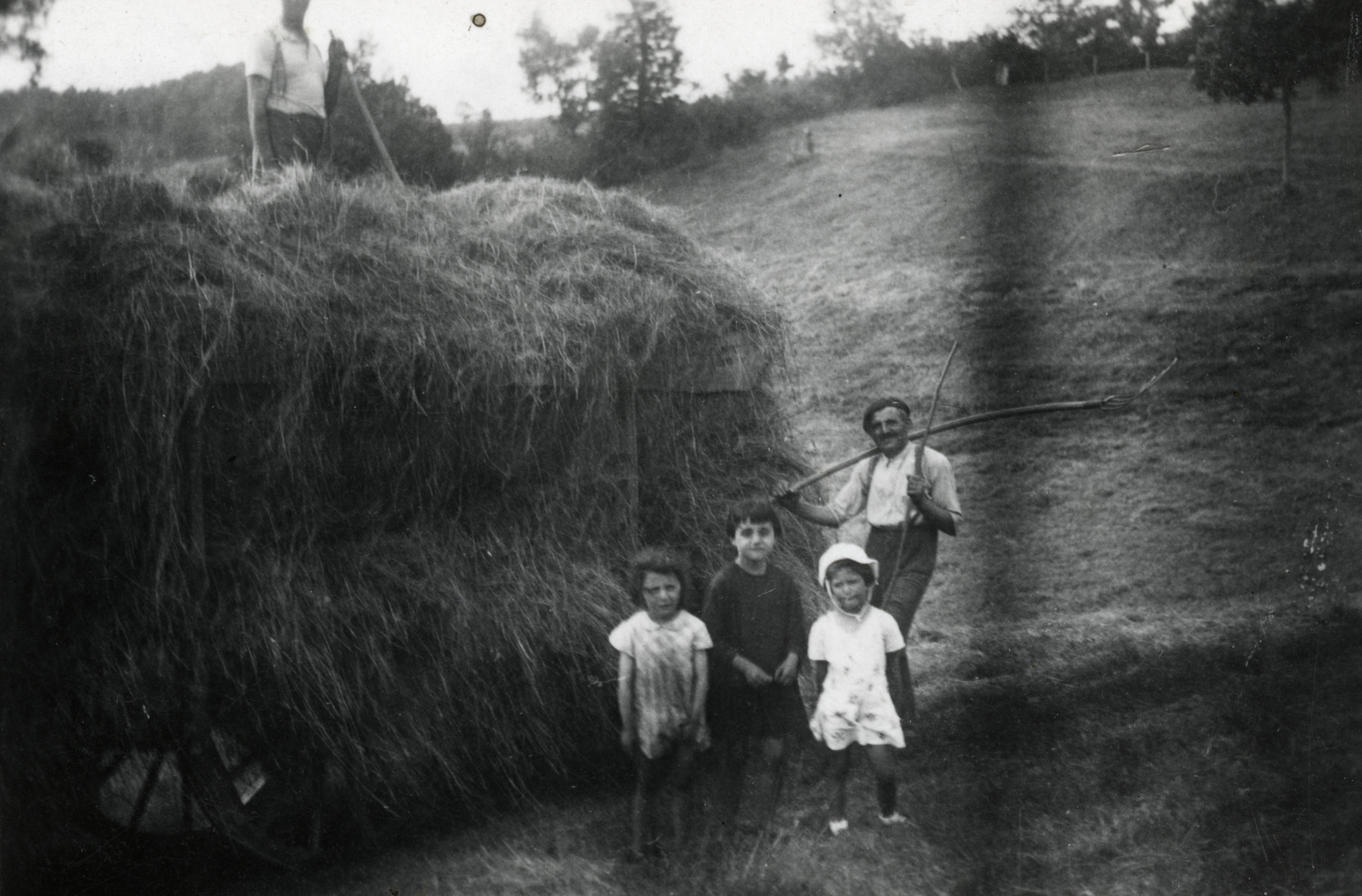 Beatrice Heffes, her father's employer Mr. Combes, and his two daughters pose in front of a haystack. Another farmer can be seen standing on top of the haystack.