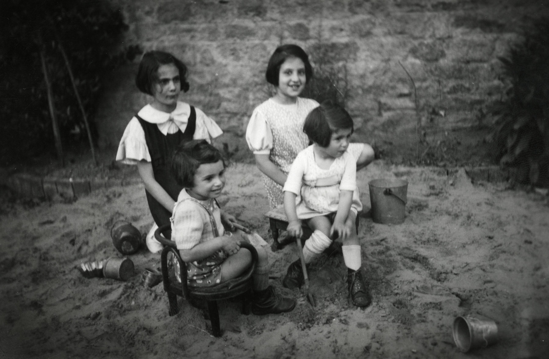 Four little girls play in the sand outside a building. Donor Beatrice Heffes is sitting at the front right.