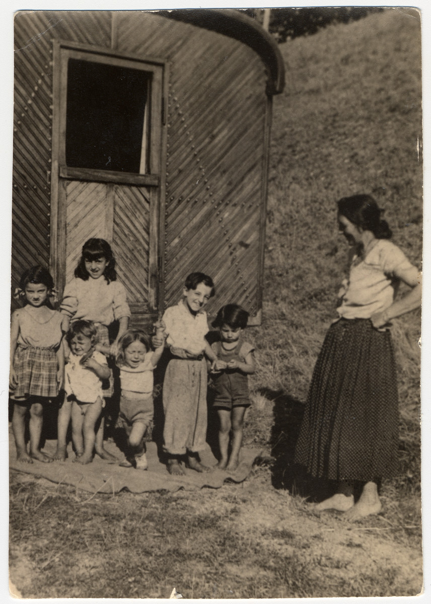 A Sinti woman stands outside of a caravan with a group of children.