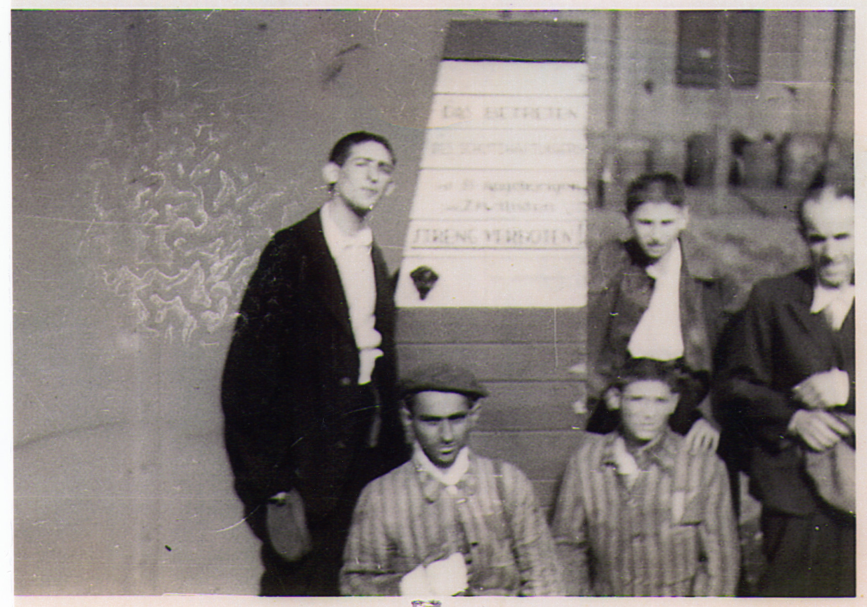 A group of survivors, including many children, stand next to a sign at the entrance to the Hanover-Ahlem concentration camp.

The German sign posted in front of the fence reads "The entrance to the prison camp by relatives of the SS and civilians is strictly forbidden."