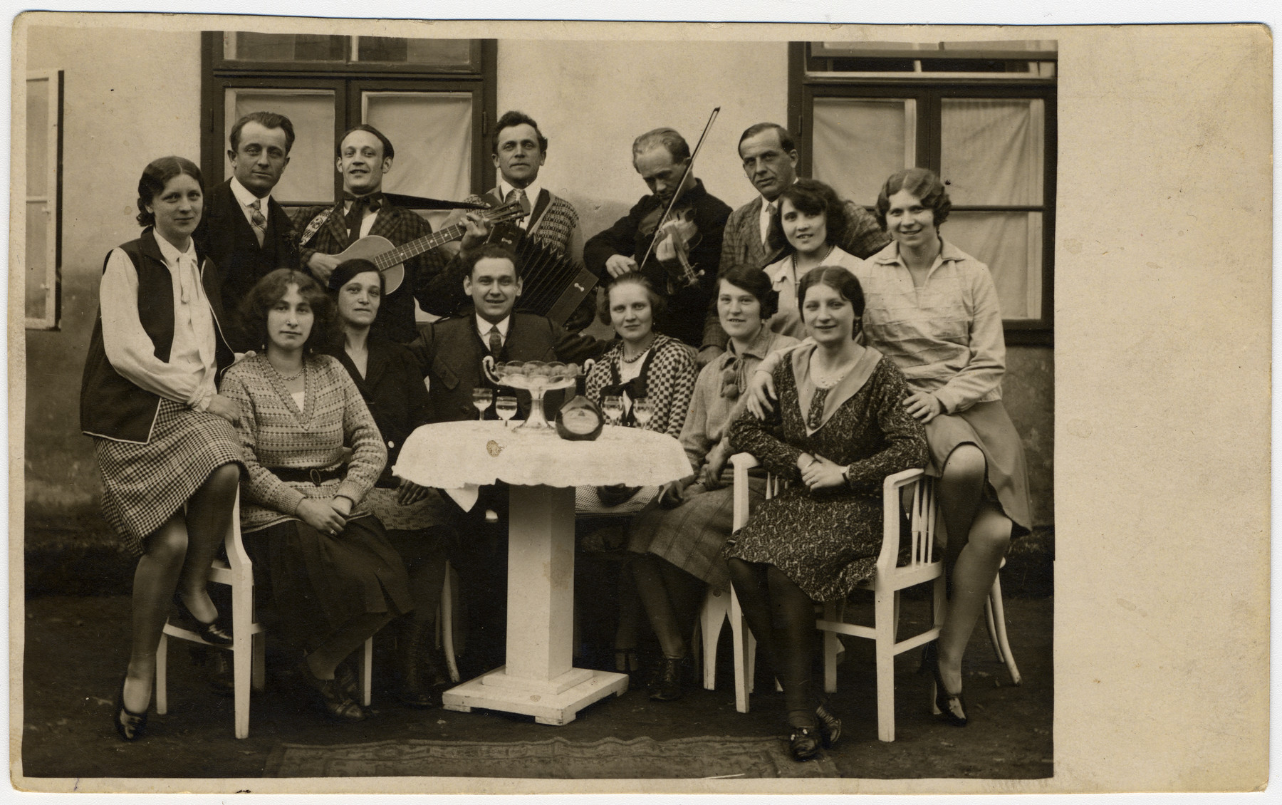 A group of friends gathers around a table, with musicians in back.

Among those pictured is Martha Holzmann (seated at  lower left).