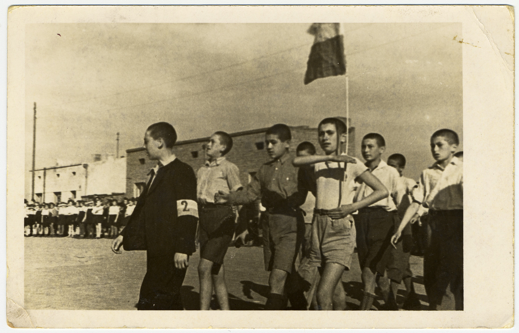 Young teenage boys, in the Marysin colony, parade with a flag, in front of Rumkowski.