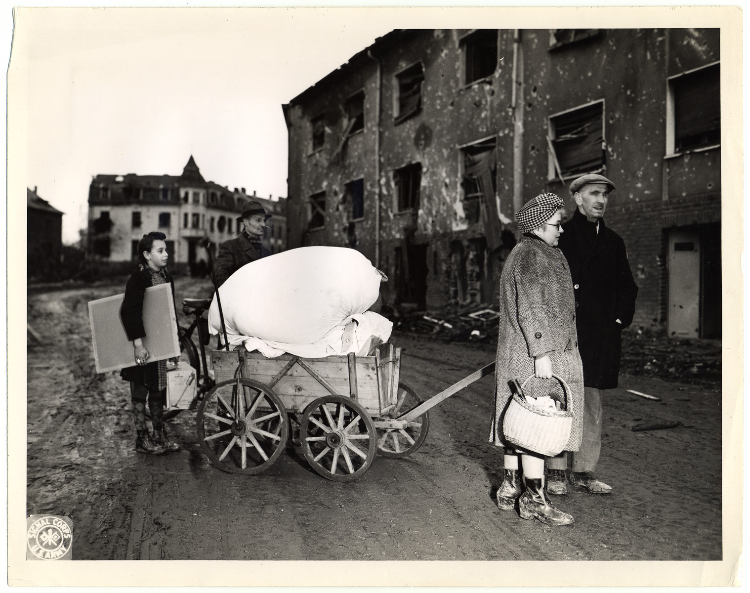 German civilians move to new quarters after their own had been damaged beyond repair.

Original Caption: "A Wurselen family moving to another house. His own was severely damaged beyond repair. The 'new' house was also damaged, but a few of the rooms could be made habitable."