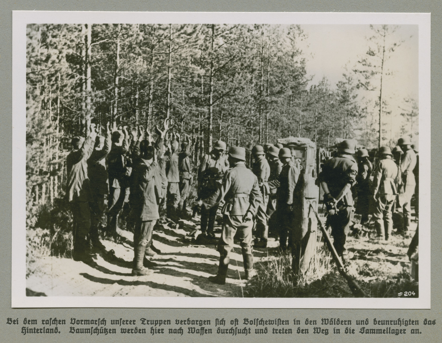 Men with their hands raised are detained by German forces.

Original Caption reads: During the rapid advance of German forces Bolshevists often hid in the forests and agitated the back country. In this image Baumschützen (forest snipers) are searched for weapons and make thier way to the detention camp.