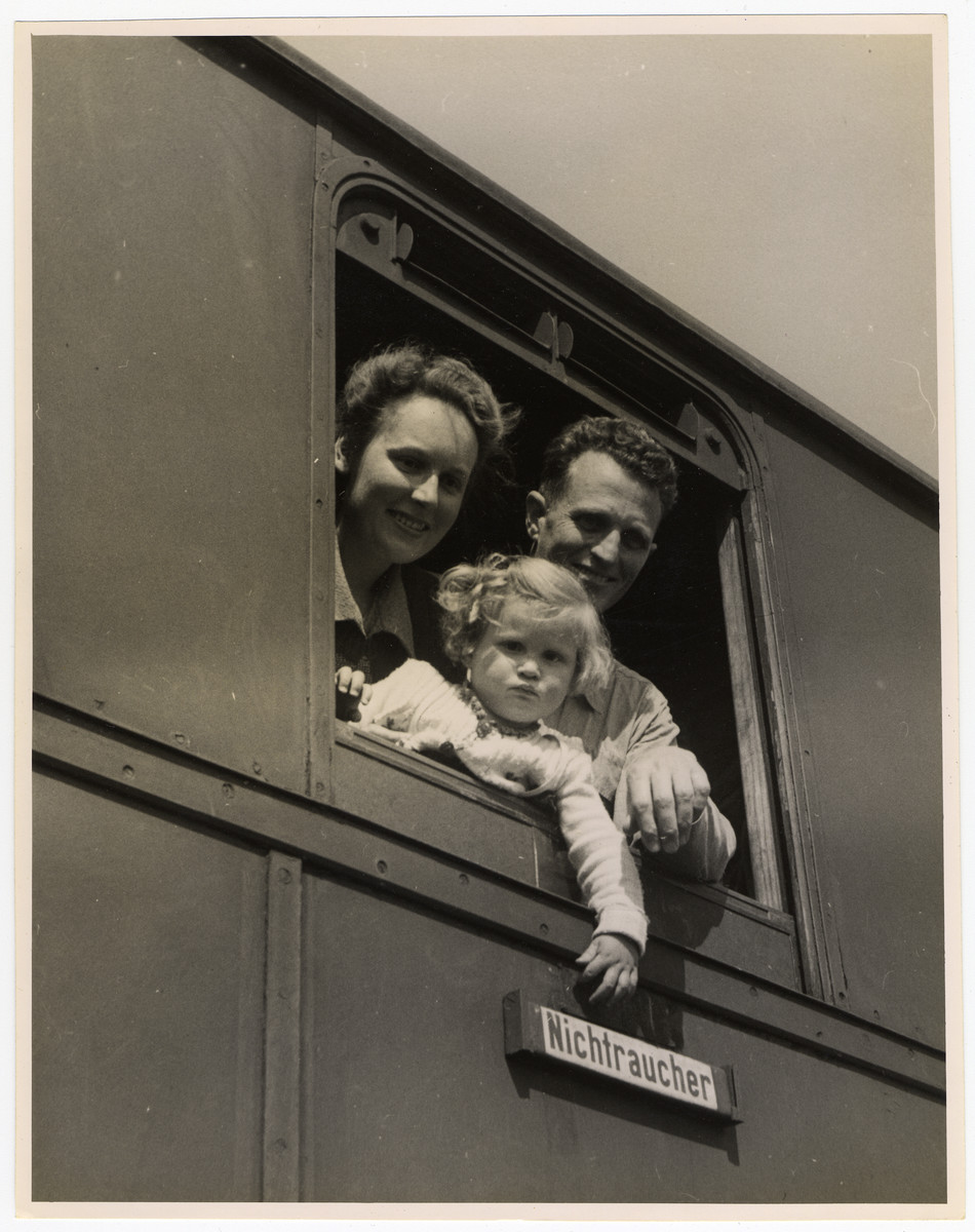 A couple and their young child look out the window of a U.S. Army train that is about to transport them from Germany.