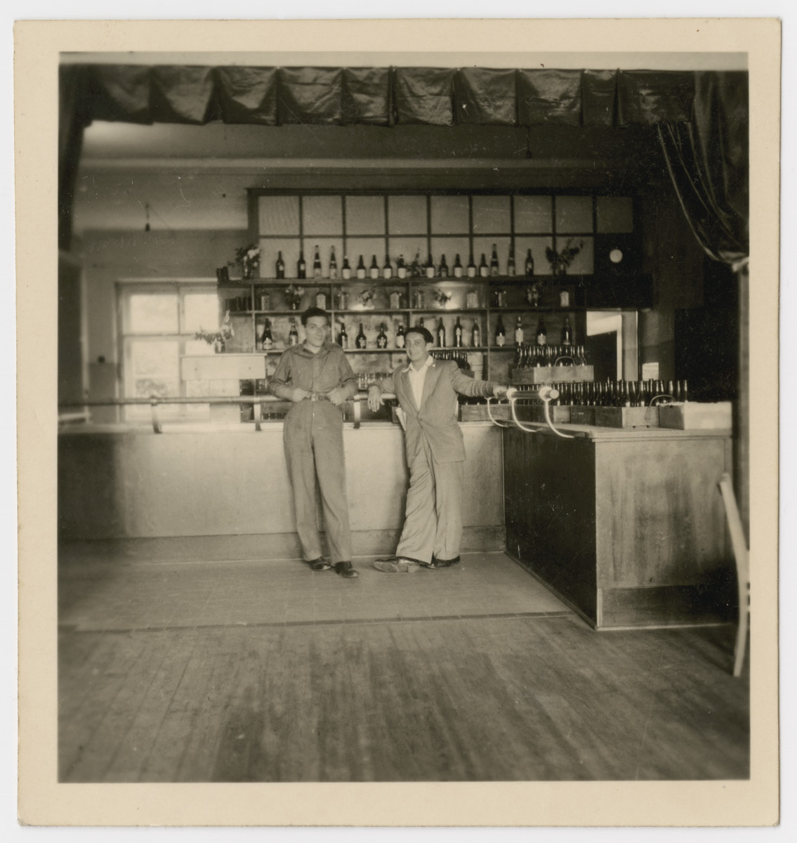 Two men pose by the bar in the Bergen-Belsen displaced persons camp.

The original caption reads: "Sam's Canteen."