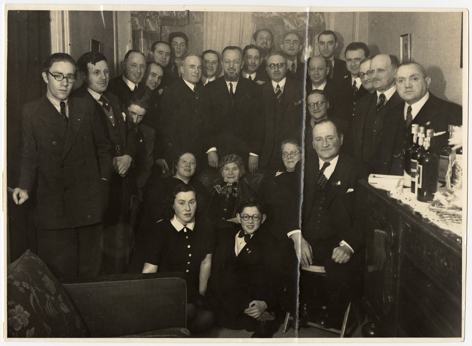 Group portrait of family and friends at a birthday celebration.  The photograph was taken on the occasion of the 75th birthday of Rosa Nachemsohn, seated in the middle. 

Among those pictured is donor's father, Herman Krogman (standing to the right of the man in the middle, with glasses).