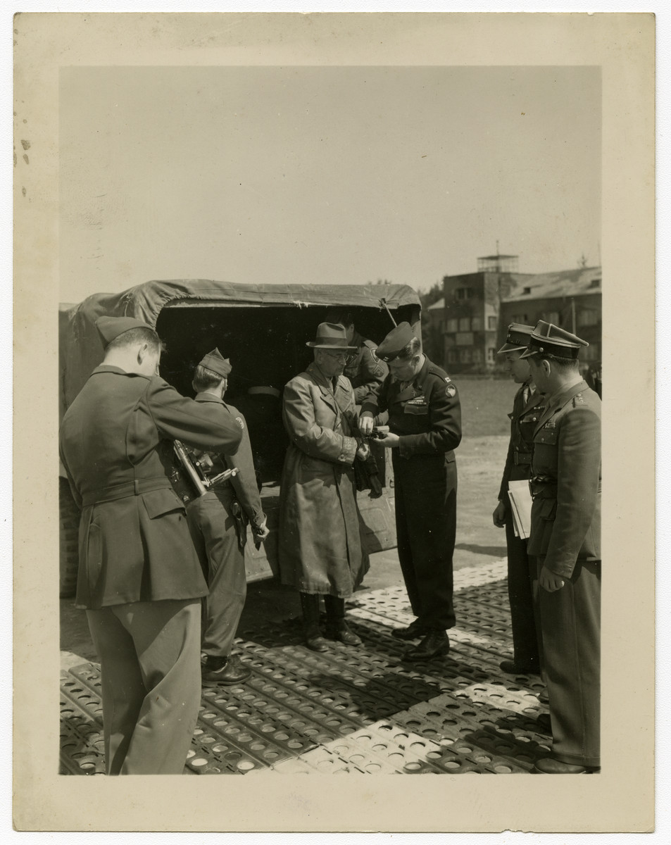Kurt von Burgsdorff is brought in handcuffs to the airport to be flown to Poland for trial as a war criminal.

Original caption reads, "Dr. Kurt Von Burgsdorff, former Governor of Kracow, Poland, under the Nazi Regime, is having his handcuffs changed by Captain Binder as two Polish officers look on. Burgsdorff, with two other Ex-Nazi officials, were being held at Nurnberg, Germany as witnesses at the International Military Tribunal trials. Burgsdorff, along with the other two men in Nurnberg, were met by seven other defendants flown from Frankfurt by the AAF Airport to Furth, Nurnberg, making a total of ten men being turned over by the Americans to the Polish Government to be tried as war criminals." 

The photo is dated 25 May and is credited to photographer PFC Eddie Murphy of the U.S. Army Signal Corps.