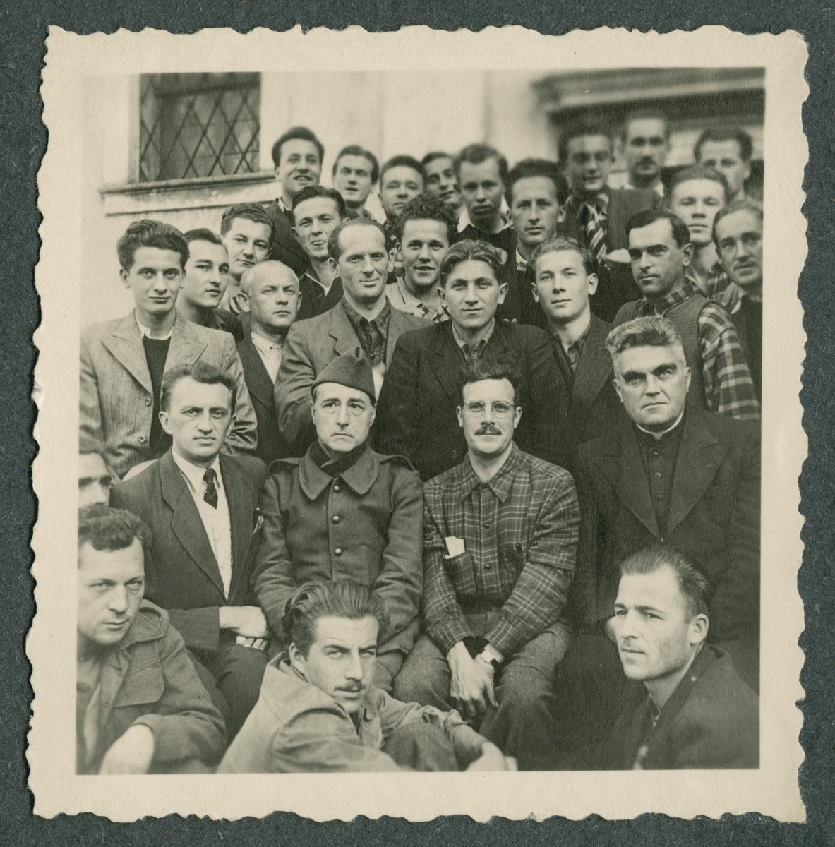 Group portrait of prisoners in Ilag VII, a camp for foreign nationals.

The man in the middle wearing the cap was a prisoner interpreter who could speak to the German authorities.  Father Sledz is in the priest's habit in the second row on the right