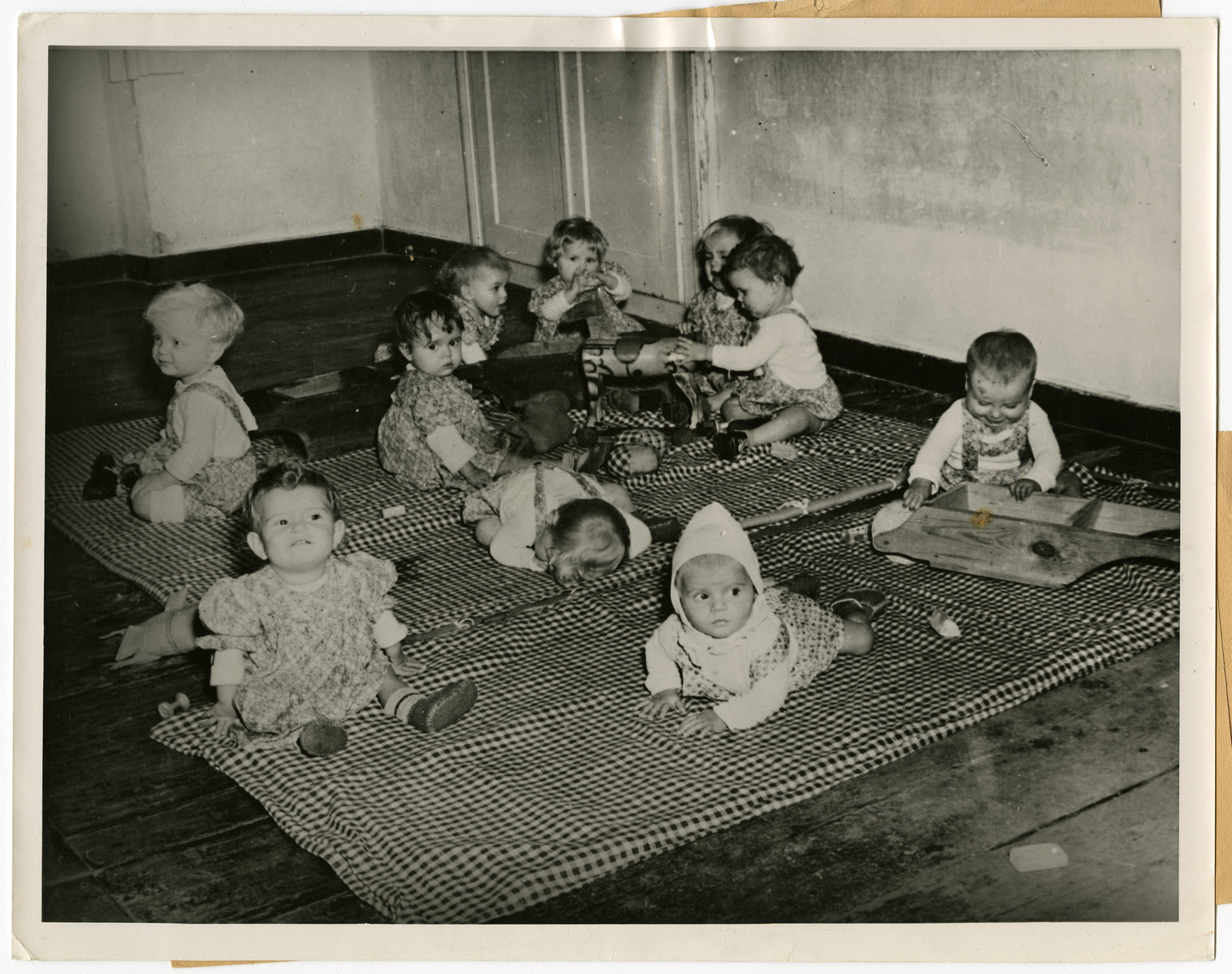 Orphans, found by U.S. troops in Germany, play in the infant/toddler room of Kloster Indersdorf.

The original caption reads: "Orphans of Indersdorf, Bavaria
Orphans of 12 nations have found a new home in a former nunnery at Indersdorf, Bavaria, where UNRRA (United Nations Relief and Rehabilitation Administration) recently opened an international refuge for children found by the U.S. Army in Germany. Hundreds of helpless children whose parents were killed or lost during the war were sent from Nazi foreign labor and concentration camps to this institution. Two- thirds of the group are Polish and Jewish. Some are too young to remember their parents and others do not know their own names. Most of these from the concentration camps have no other identification than a number and the letters "KL" (Konzentrations Lager) marked on their skins. When children arrive at the institution, they are deloused, bathed and given clean clothes. Medical attendants then innoculate them against typhoid fever, diptheria, and smallpox. The infants are cared for by nurses while older children begin elementary education in their own language under teachers of the Allied nations. 

This photo shows: Orphan children, found by the U.S. troops advancing into Germany during the war, frolic happily in the playroom of the institution."