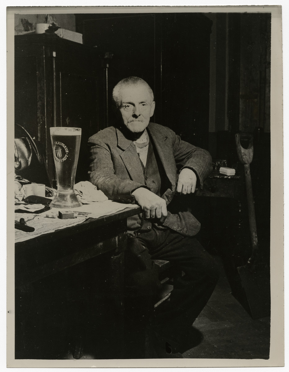 Wilhelm Guillion, a janitor of a beer hall, poses at the table where Hitler first laid plans for the formation of the Nazi Party. 

Original caption on the back of the photo reads:
Nazi Meeting Place
Wilhelm Guillion, 76-year-old civilian of Munich, sits at a table where Hitler first laid plans for the formation of the Nazi Party. Guillion is a janitor of a building containing one of the beer houses where the original Nazi Party meetings were held. In the cabinet behind him, many original Hitler documents regarding the party's formation were found. Munich, which was the scene of Hitler's abortive beer cellar "putsch" in 1923, was captured April 29, 1945, by troops of the Seventh U.S. Army. Associated Press Photo.