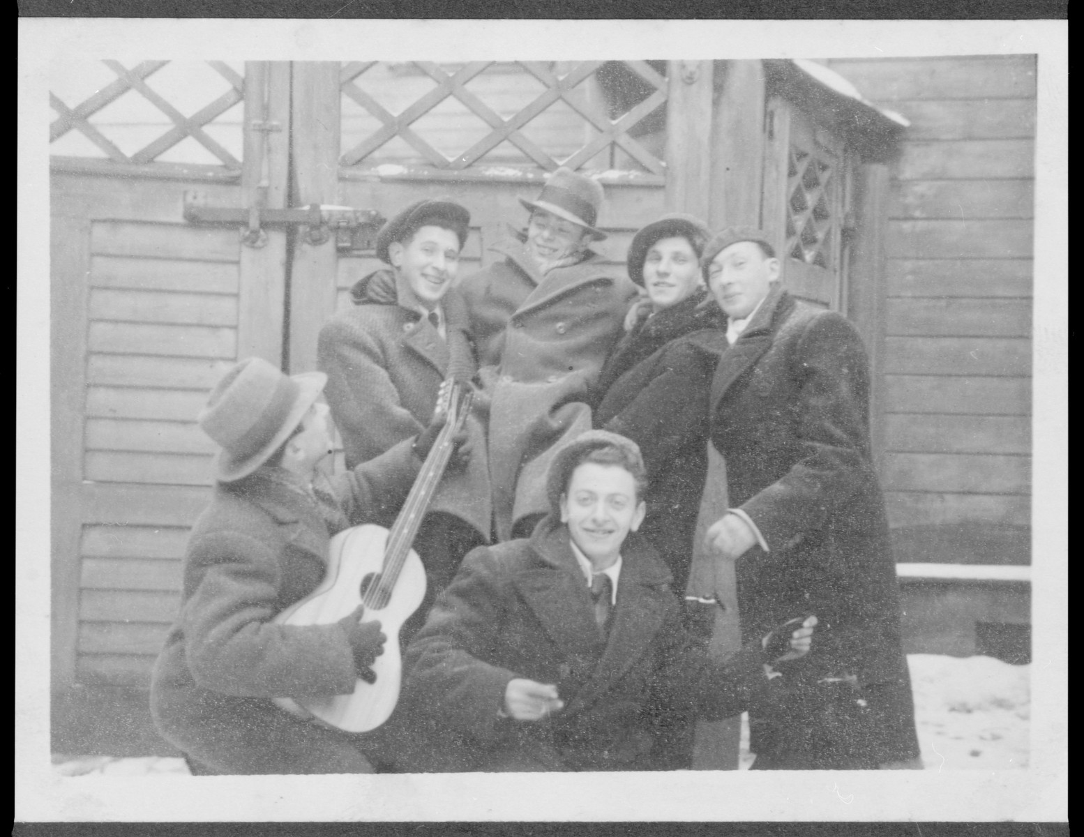 A group of Latvian Jewish friends, one playing the guitar, poses outside a building in the snow.

Pictured in the back center is Elja Heifecs.