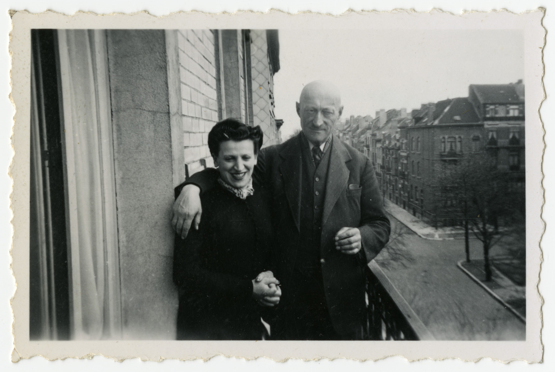 Frajdla Birnbaum stands on her apartment balcony next to an older gentleman [possibly her father-in-law Joseph Birnbaum].