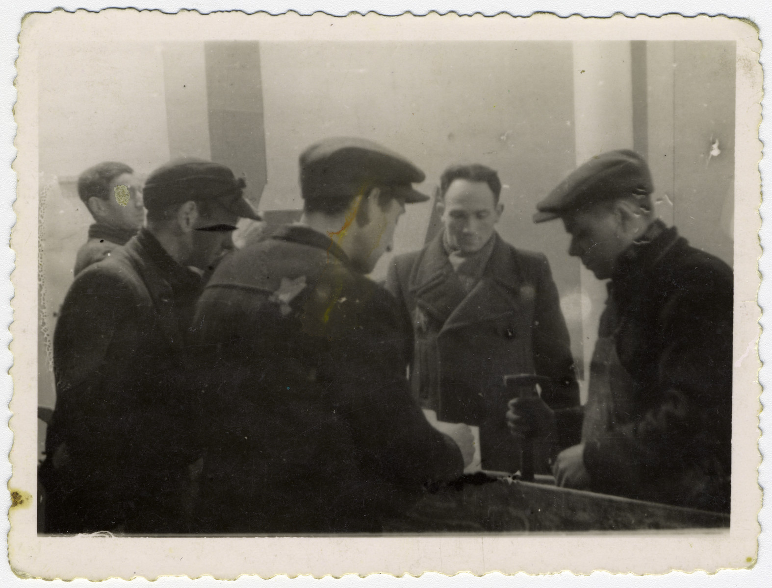 A group of Jewish men discuss their work in one of the Lodz ghetto workshops. 

Among those pictured, third from the left with the hat, is donor's brother-in-law, Josef Szwarc (later Schwartz).