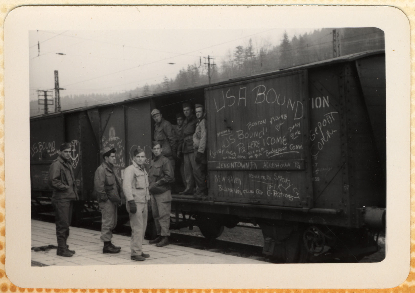 American GIs prepare to return home.  They are standing by a train with the words "USA Bound" written on its side.