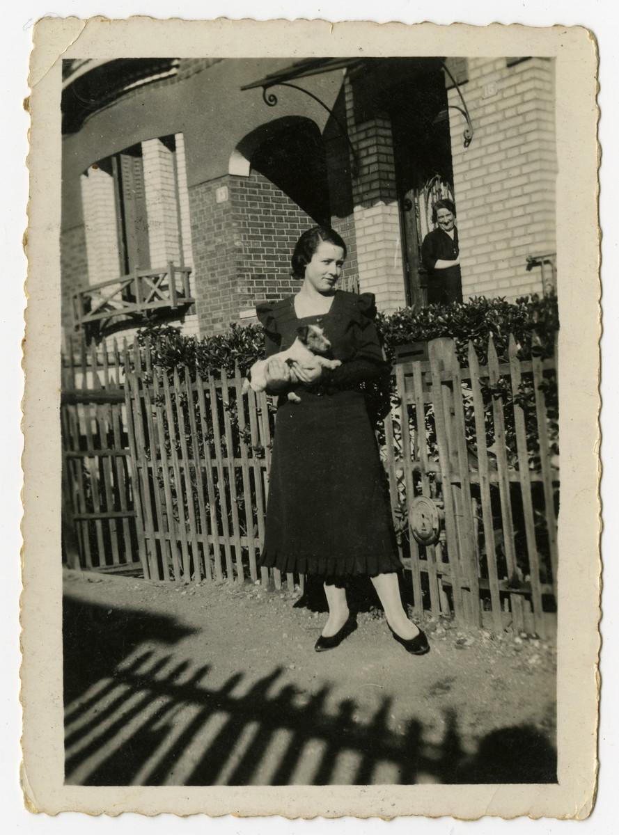 A woman holding a puppy stands outside a house [probably ra elative of Izak Weber in Skole, Poland.]