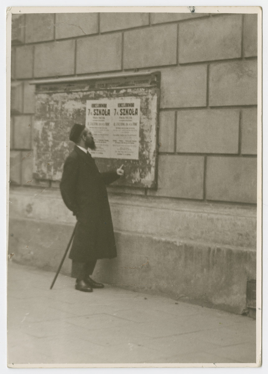 A religious Jew studies a Polish bulletin about a school pasted on the wall of a building.

Photograph is used on page 146 of Robert Gessner's "Some of My Best Friends are Jews."