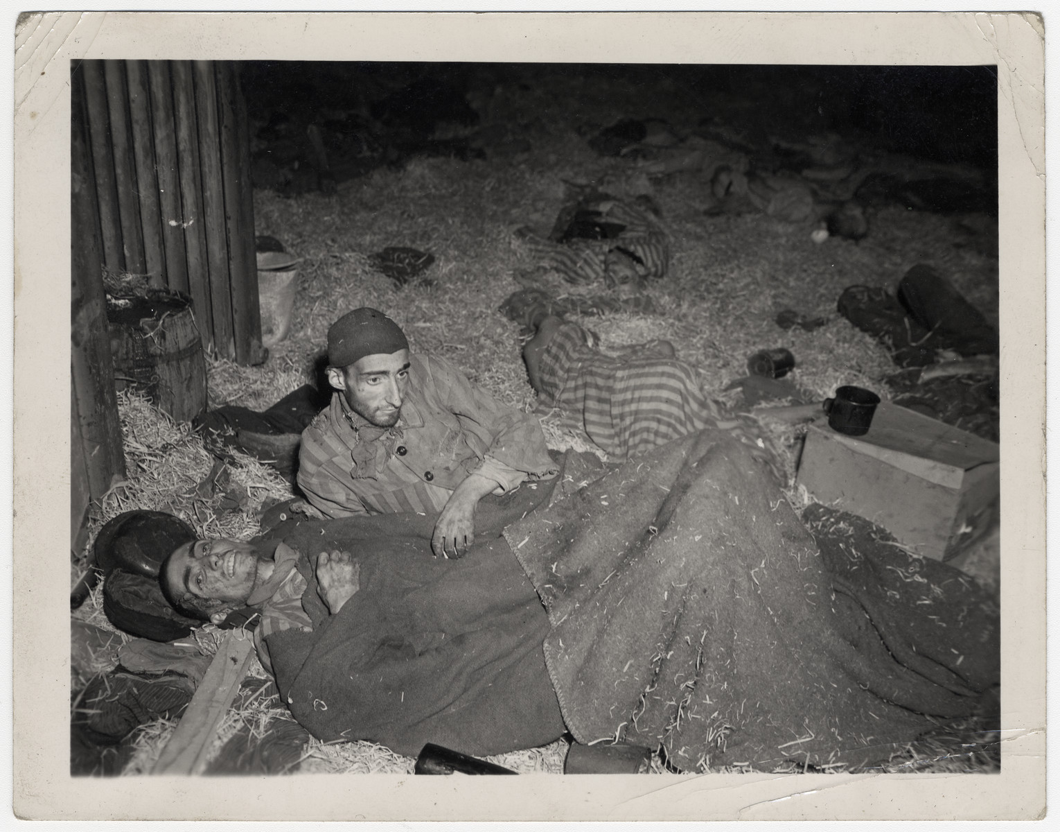 Two survivors lie down on the straw inside a barrack in Nordhausen.
