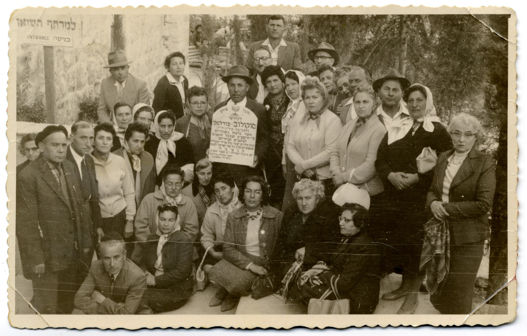 Survivors of Sokolow Podlaski pose around a makeshift tombstone during a memorial service for the Holocaust victims of the town.

Shoshana Feldman (sister of Mendel) is among those pictured.  She immigrated to Palestine before the war is part of the group.

Also pictured is Srul Szczerb, seen  holding the plaque. His sister, Malka  (Szczerb) Goldschmidt  is standing to his right (wearing a scarf and glasses). The two survived the war in Russia and then immigrated to Israel afterwards.  Their younger sister, Cywia (Szczerb) Elster, had been hiding in the farms around the town of Sokolow and was turned in to the Germans by a farmer named Oziemblo six months before the end of the war. The Germans brought her into the town and then shot her. Cywia's children,  Irene  and Aaron Elster survived.